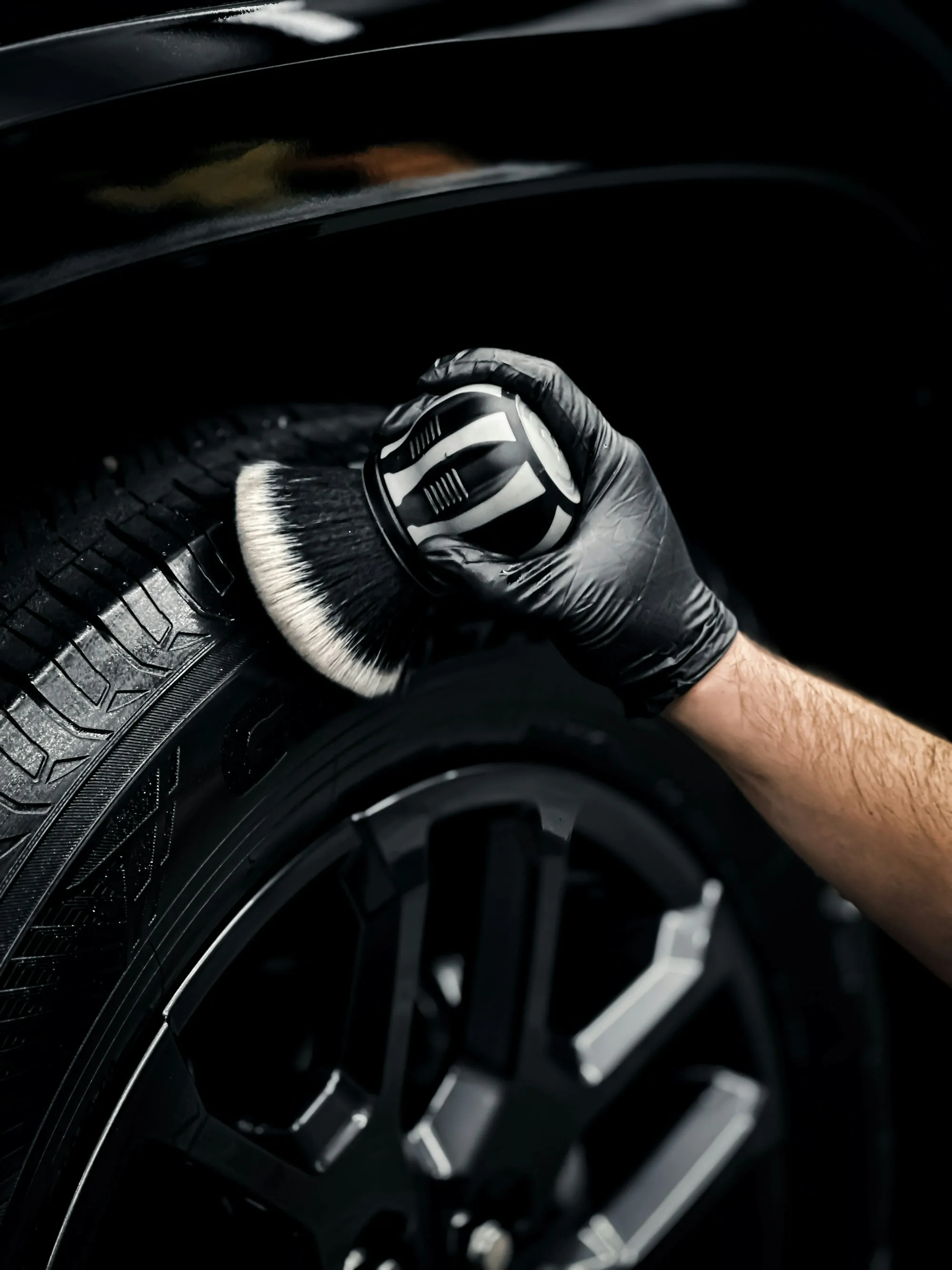 Gloved hand cleaning a car wheel with a soft brush