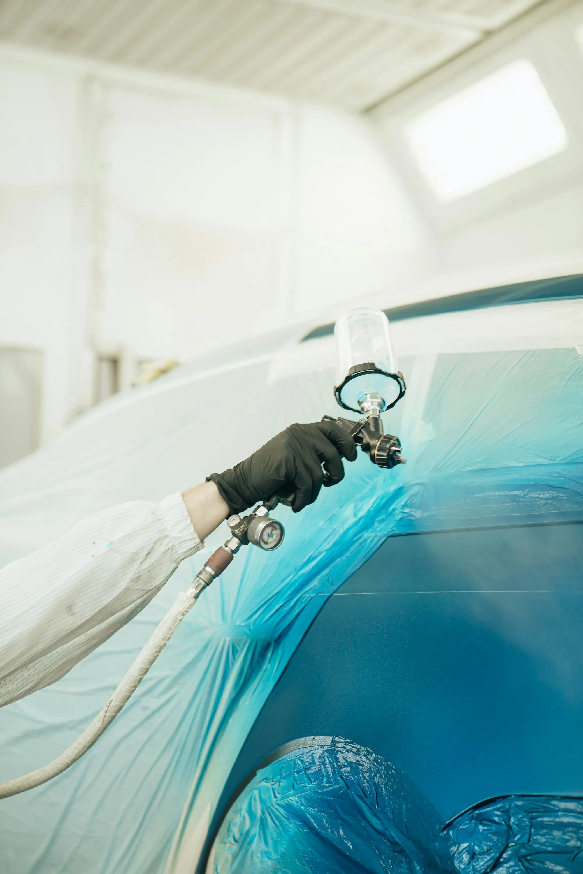 Painter spraying a fresh coat on a blue car panel